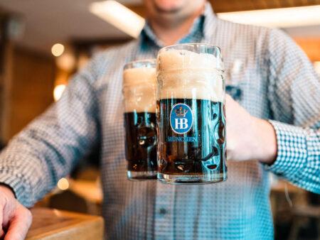 Eine Hand hält zwei Bierkrüge mit dunklem Bier.